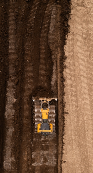 Aerial view directly above a bulldozer or earth moving machine with tracks pushing earth and soil in the construction industry on a brownfield site with copy space